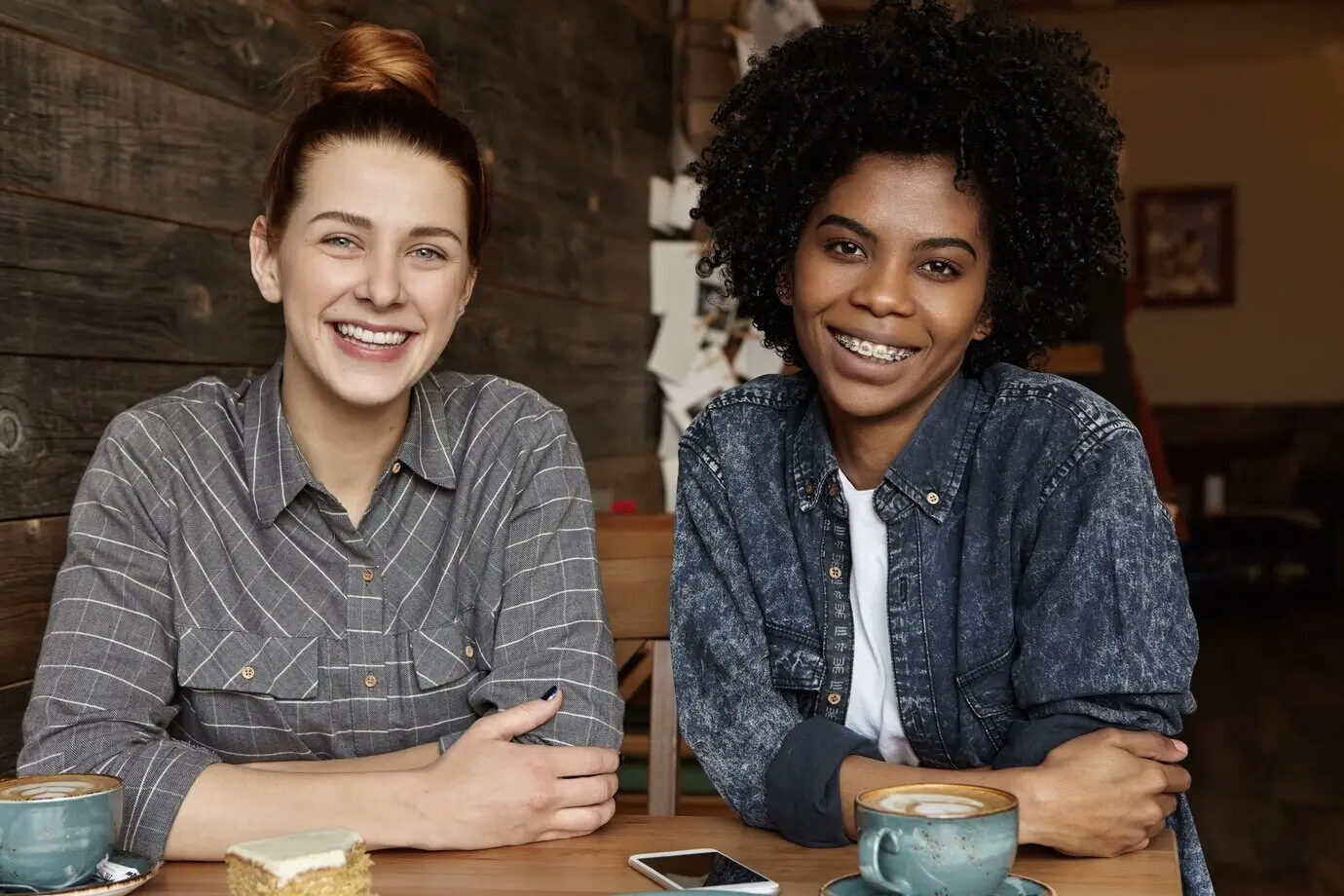 Dos lesbianas felices tomando café, sentadas a una mesa en un restaurante acogedor.